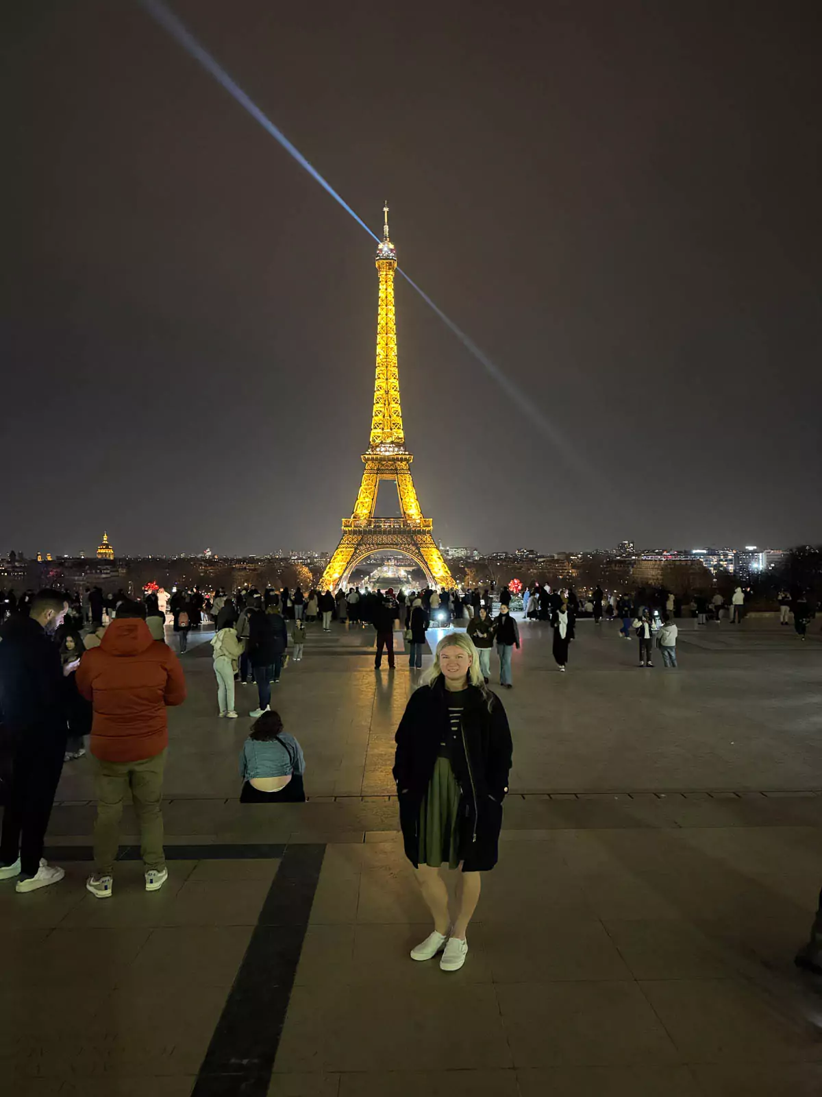 Katie standing at the Trocadéro in Paris, France, gazing at the Eiffel Tower illuminated against the night sky, with the tower’s golden lights casting a romantic glow — a dreamy scene
