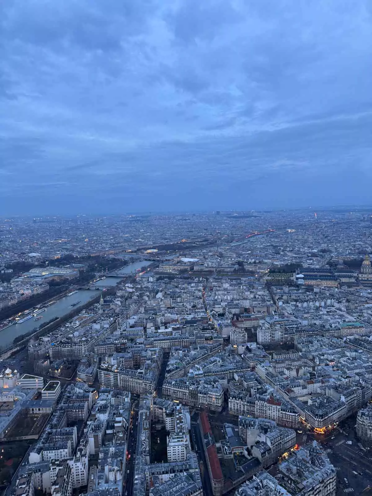 Expansive view from the top of the Eiffel Tower in Paris, France, showing the city’s iconic rooftops, the Seine River, and distant landmarks under a soft, hazy sky — a breathtaking panorama