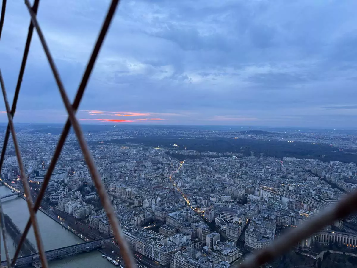 Panoramic view from the top of the Eiffel Tower in Paris, France, capturing the city’s sweeping skyline with the Seine River, historic rooftops, and distant landmarks under a hazy sky — an unforgettable vista