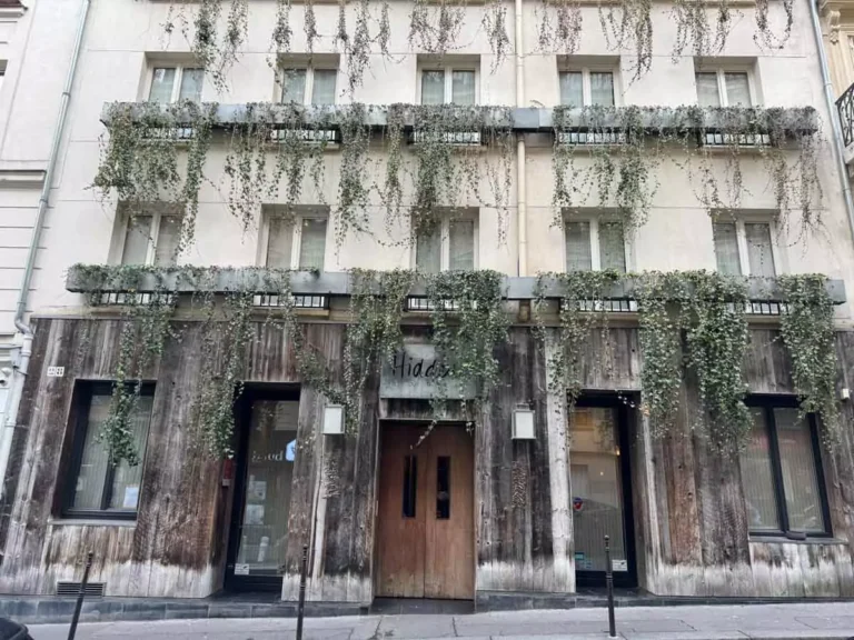 Charming exterior of hidden hotel in Paris, France, tucked along a quiet street with ivy-covered walls, vintage lanterns, and classic Parisian architecture — a tucked-away gem