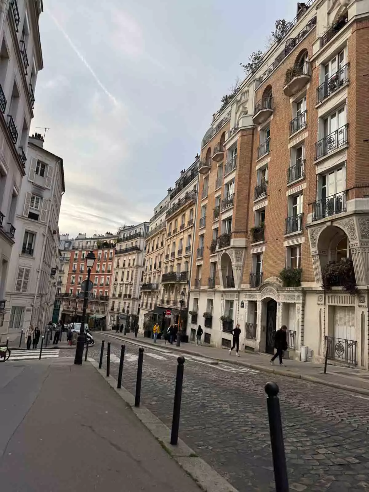 Scenic view of Montmartre in Paris, France, featuring charming cobblestone streets, classic Parisian buildings with wrought-iron balconies, and artists setting up easels in the square. The artistic atmosphere and hillside setting reflect the neighborhood’s bohemian spirit.