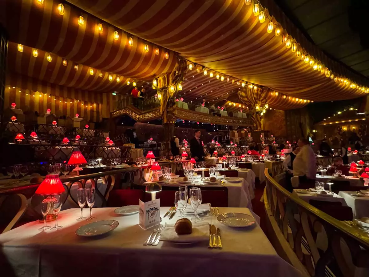 View of balcony seating inside the Moulin Rouge in Montmartre, Paris, with tables arranged along ornate railings, offering an elevated view of the stage in the historic red-and-gold cabaret interior.