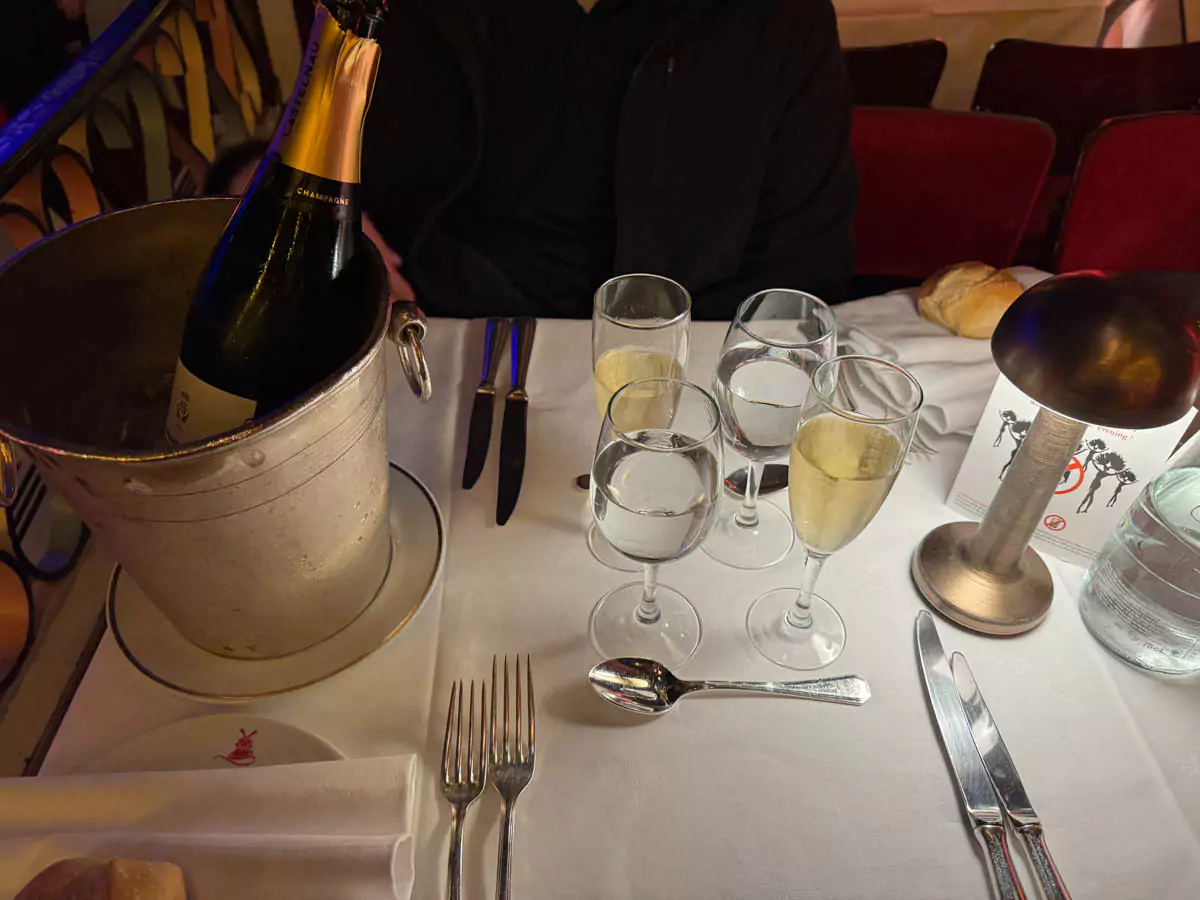 Bottle of champagne on a table at the Moulin Rouge in Montmartre, Paris, accompanied by two filled flutes, capturing a festive moment in the iconic cabaret’s glamorous setting.