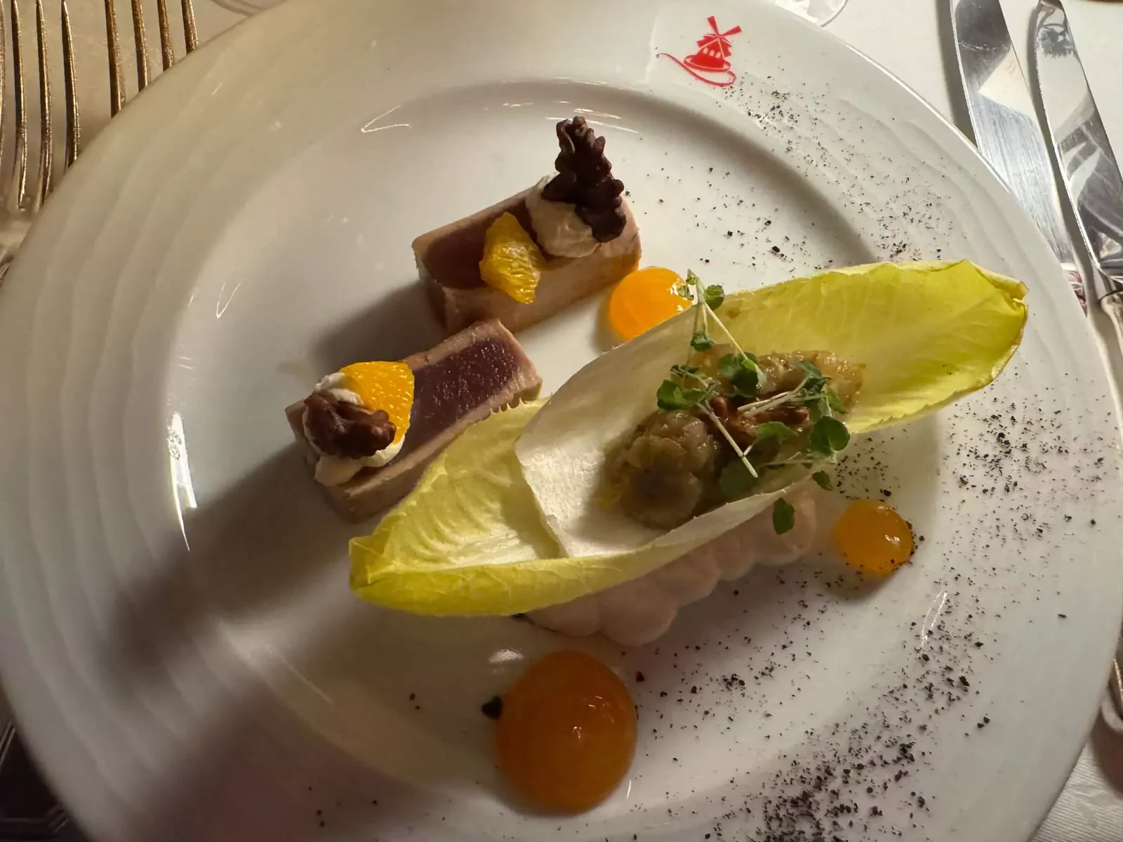 Saku tataki tuna flavored with citrus fruits, served with textured endives, horseradish cream, and caramelized walnuts, artfully plated at the Moulin Rouge in Paris for a sophisticated starter.