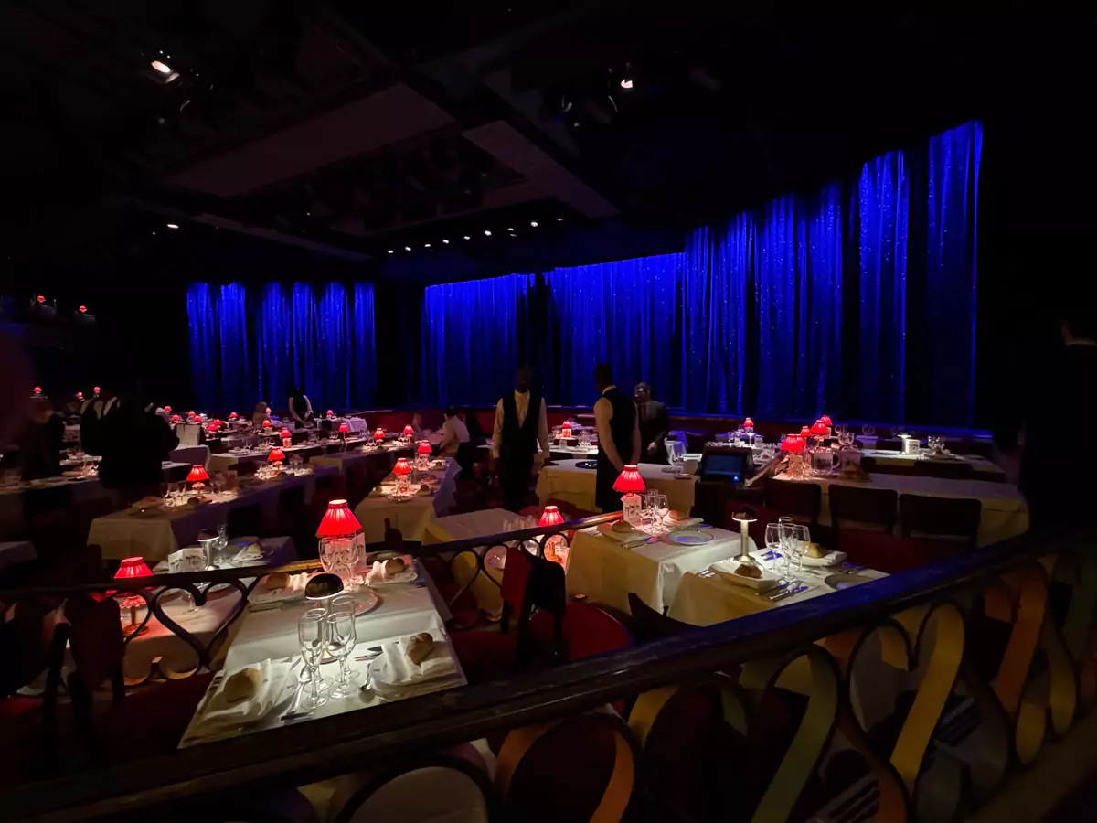 Inside view of the Moulin Rouge in Montmartre, Paris, showing dinner tables set with red lamps and white linens, all facing the grand stage where the famous cabaret performances take place.