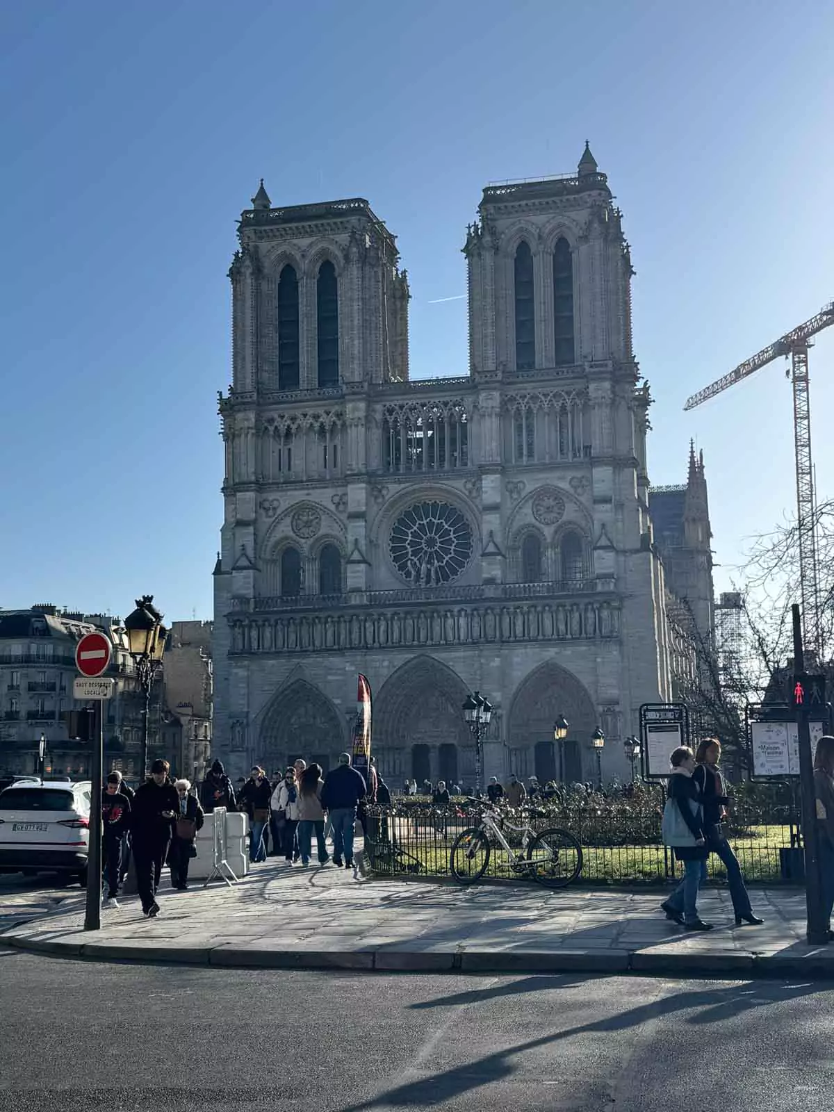 Front exterior of Notre-Dame Cathedral in Paris, France, showcasing its iconic Gothic façade with twin towers and rose window, as crowds of tourists gather in the square below on a clear day.