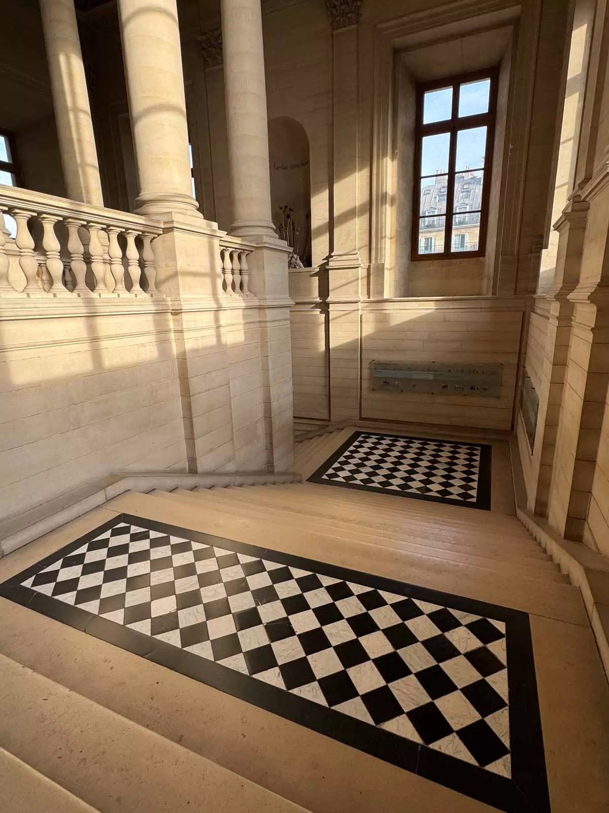 The Escalier Nord de la Colonnade at the Louvre Museum in Paris, France, featuring a grand staircase framed by classical columns, stone balustrades, and soft natural light — an elegant architectural feature