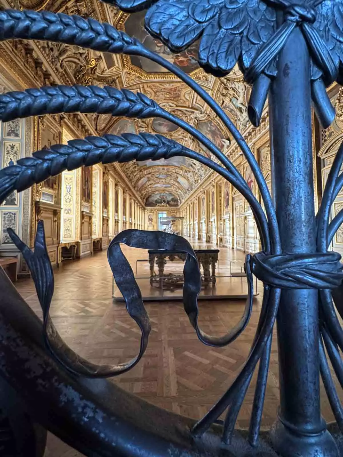 View into the Galerie d’Apollon at the Louvre Museum in Paris, France, seen through ornate golden gates, revealing a richly decorated hall with gilded ceilings, chandeliers, and classical paintings — a glimpse of regal splendor