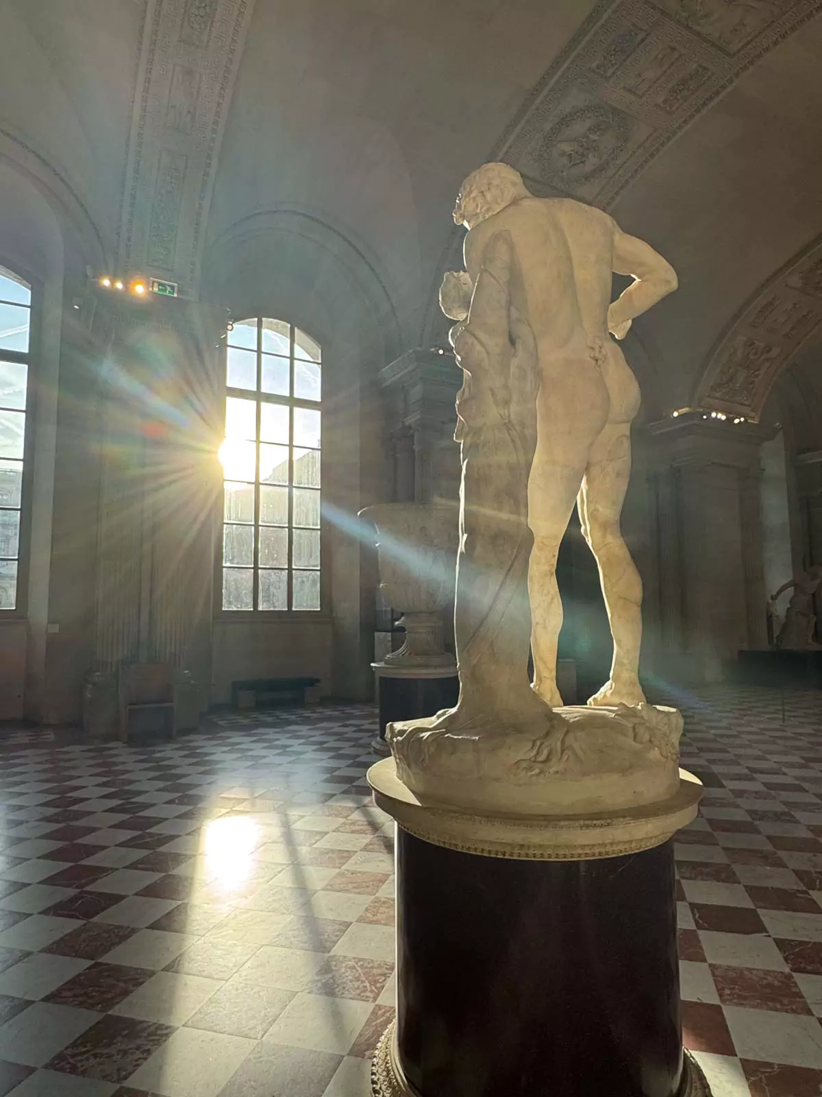 Greek statue at the Louvre Museum in Paris, France, illuminated by soft natural light streaming through a tall window, highlighting the marble contours and serene expression — a quiet, timeless moment