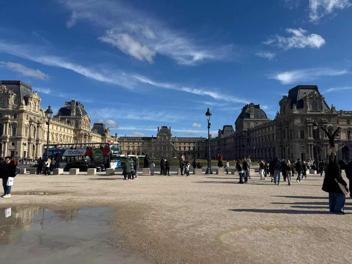 Tootbus parked near the Louvre Museum in Paris, France, with the iconic palace façade in the background and tourists boarding the open-top sightseeing bus — a convenient and scenic stop