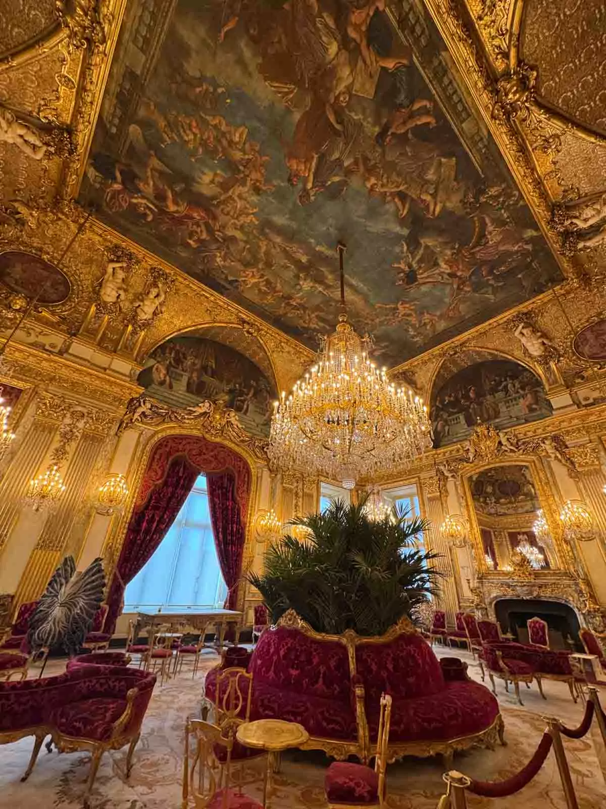 The Napoleon III Apartments at the Louvre Museum in Paris, featuring lavish chandeliers, gilded moldings, plush red furnishings, and ornate ceilings — a richly decorated space reflecting imperial luxury