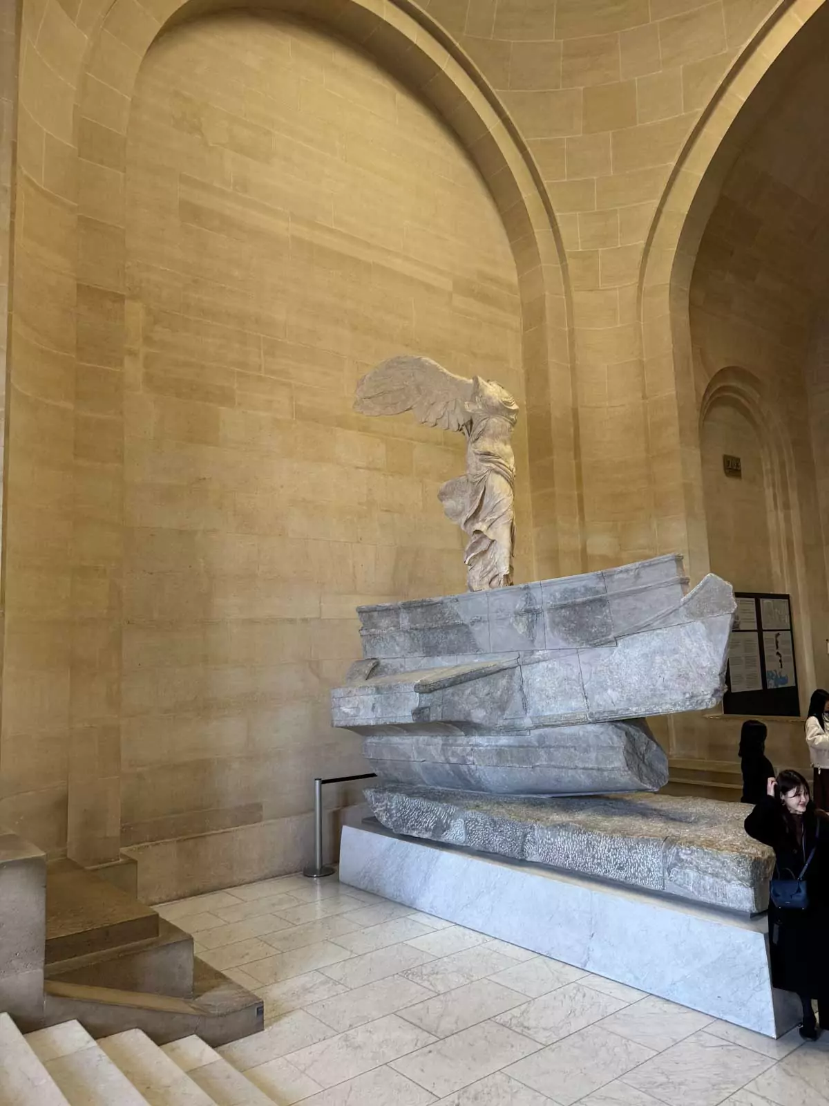 The Winged Victory of Samothrace at the Louvre Museum in Paris, France, displayed atop a marble staircase with dramatic lighting accentuating the flowing drapery and powerful stance of the ancient Greek sculpture — an iconic masterpiece