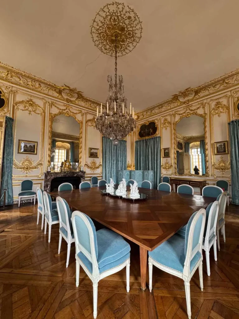 The Salle à Manger aux Retours de Chasse (Post-Hunt Dining Room) at the Palace of Versailles, with a richly set table, game-themed decor, gilded paneling, and paintings celebrating royal hunting traditions — a lavish and thematic space