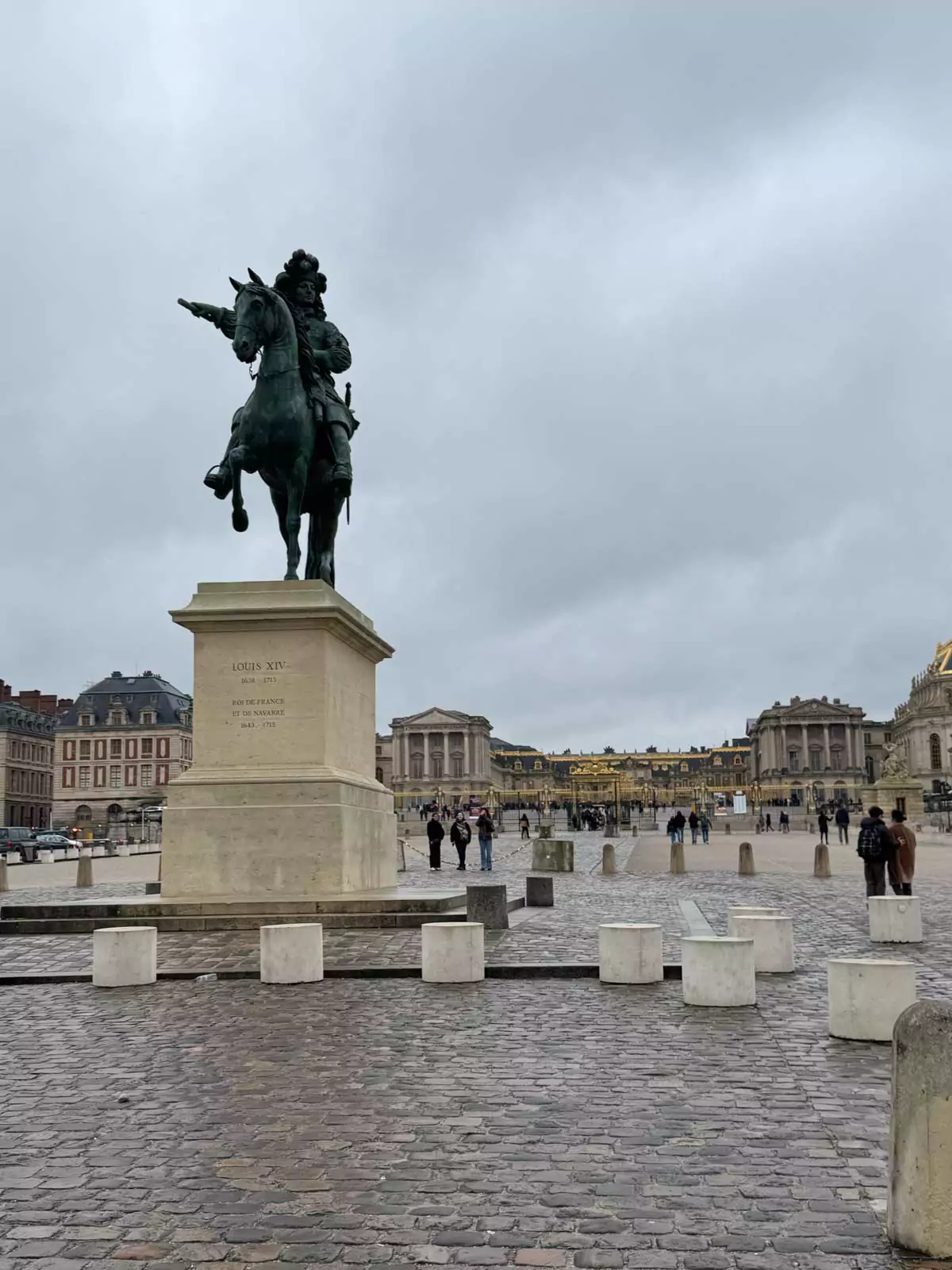 Equestrian statue of Louis XIV at the Palace of Versailles, France, depicting the Sun King in bronze on horseback, set against the grand château’s forecourt and dramatic sky