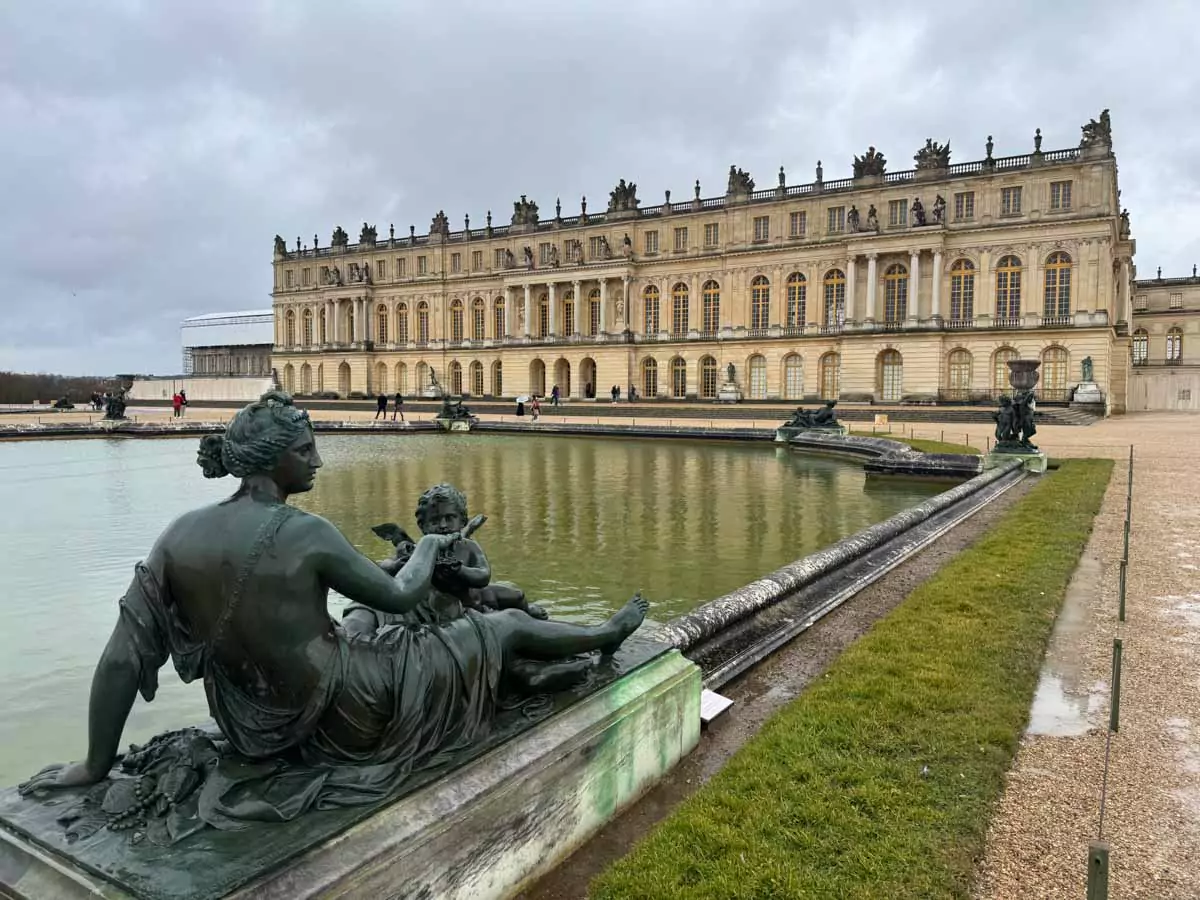 Garden statue beside a reflective pond at the Palace of Versailles in Paris, France, featuring a classical marble figure surrounded by trimmed greenery and calm waters mirroring the formal landscape — a peaceful corner