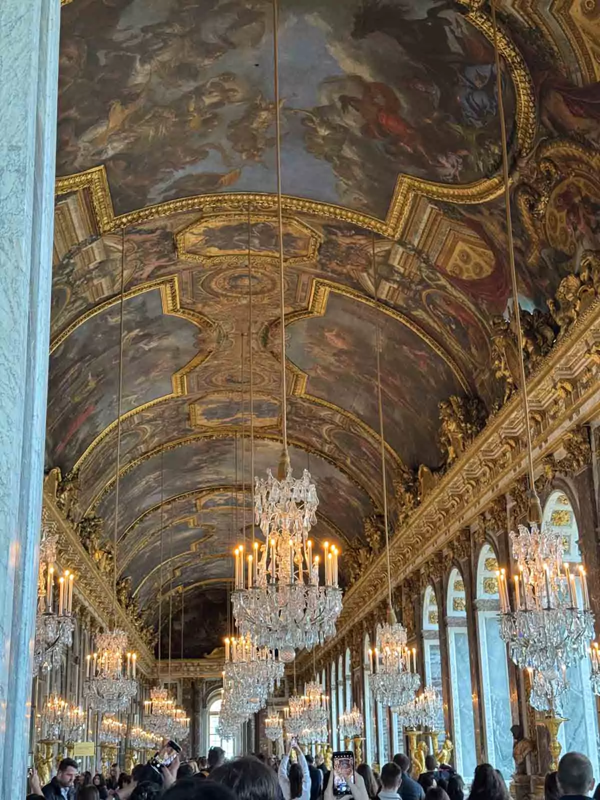 The Hall of Mirrors at the Palace of Versailles in Paris, France, featuring glittering chandeliers, arched mirrors reflecting golden light, and ornate baroque ceiling paintings