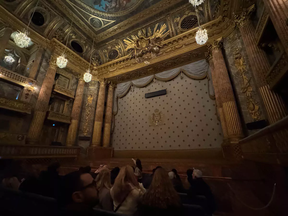 The stage of the Opéra Royal de Versailles in Paris, France, with its ornate proscenium arch, rich blue and gold detailing, and elegant chandeliers casting a warm glow