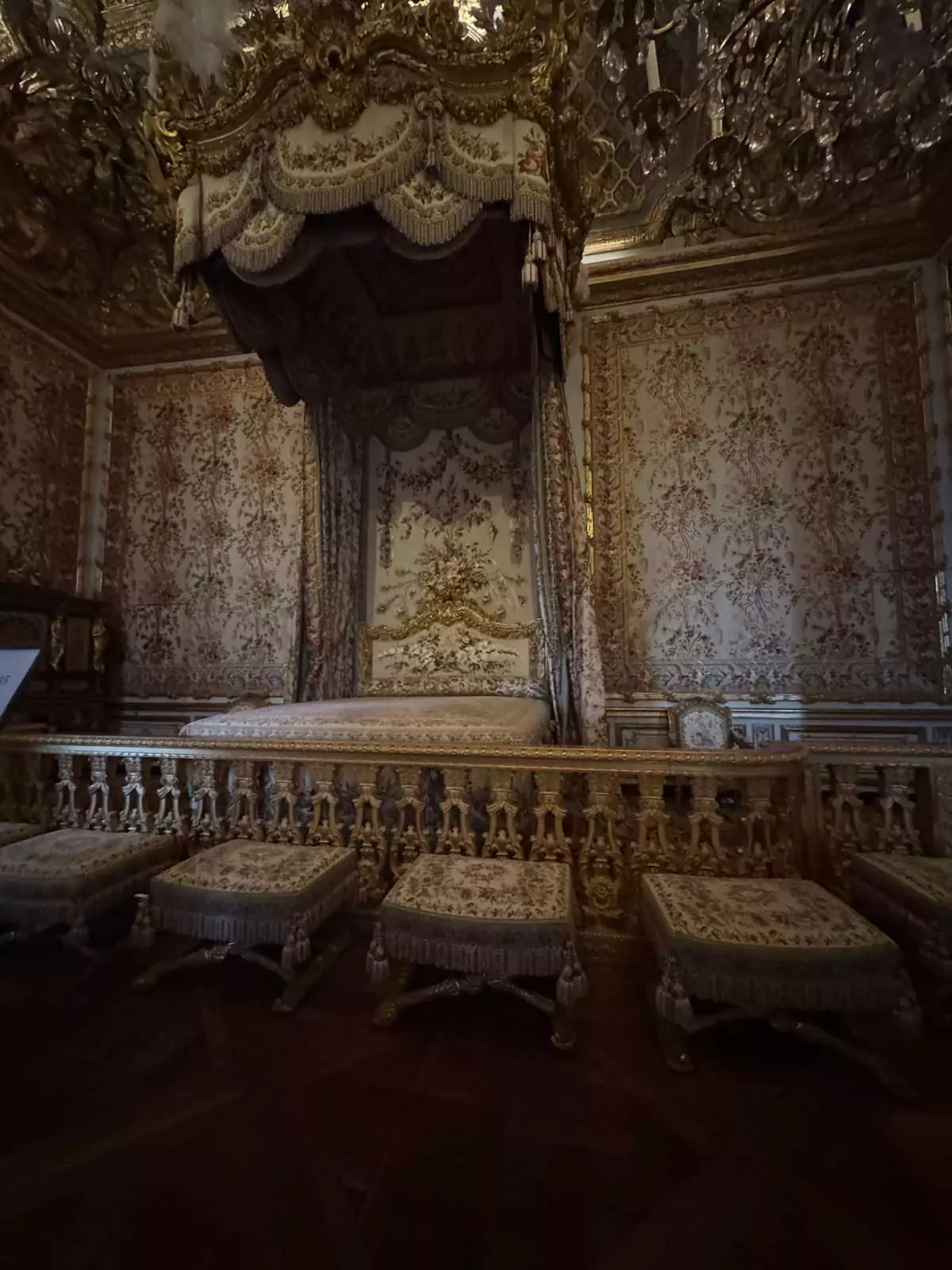 The Queen’s bedroom in the Palace of Versailles, Paris, France, showcasing a lavish canopy bed with floral fabrics, gilded woodwork, and Rococo-style decor