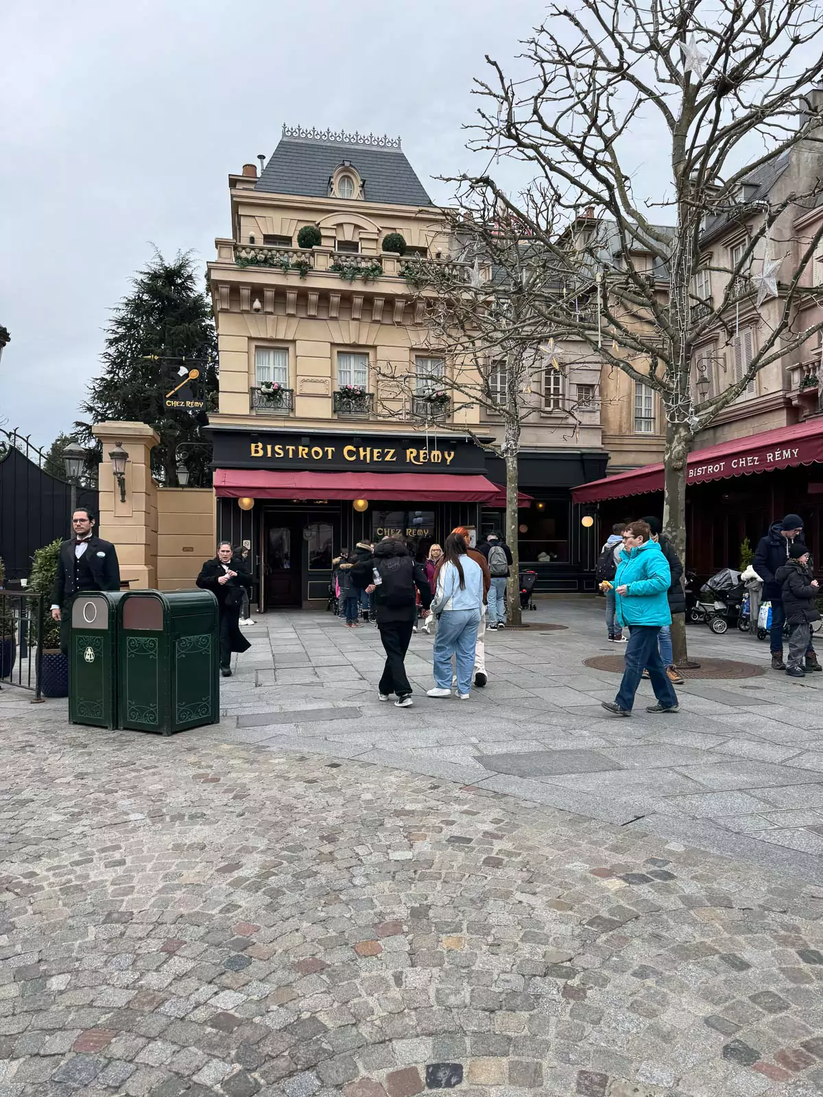 Entrance to Bistrot Chez Rémy at Disneyland Paris, featuring a whimsical oversized sign, lush greenery, and Parisian-style details inspired by the movie Ratatouille, creating a cozy, storybook atmosphere.