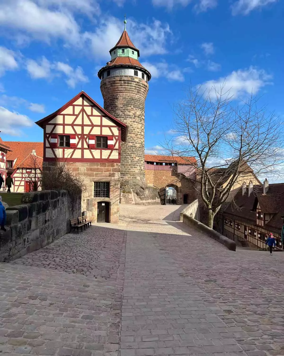 Interior view from within the Imperial Castle of Nuremberg, Germany, showing medieval stone walls, timber-framed structures, and a cobblestone courtyard framed by historic towers.