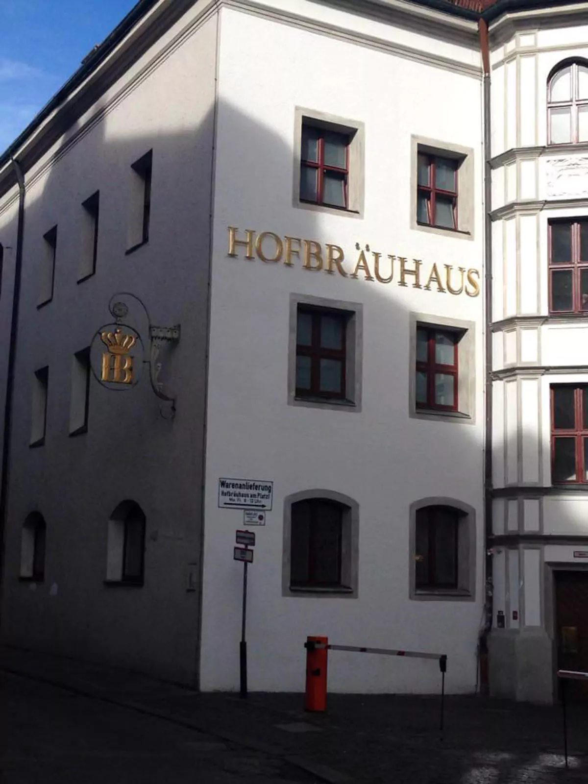 The historic Hofbräuhaus building in Munich with its traditional Bavarian architecture, featuring white walls, decorative window shutters, and a prominent sign above the entrance. The bustling street in front shows visitors arriving at one of the city’s most famous beer halls.