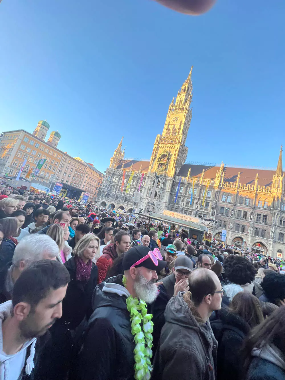 A bustling Marienplatz square in Munich filled with a dense crowd of people celebrating Carnivale. Colorful costumes and festive decorations create a lively and energetic atmosphere in the historic city center.