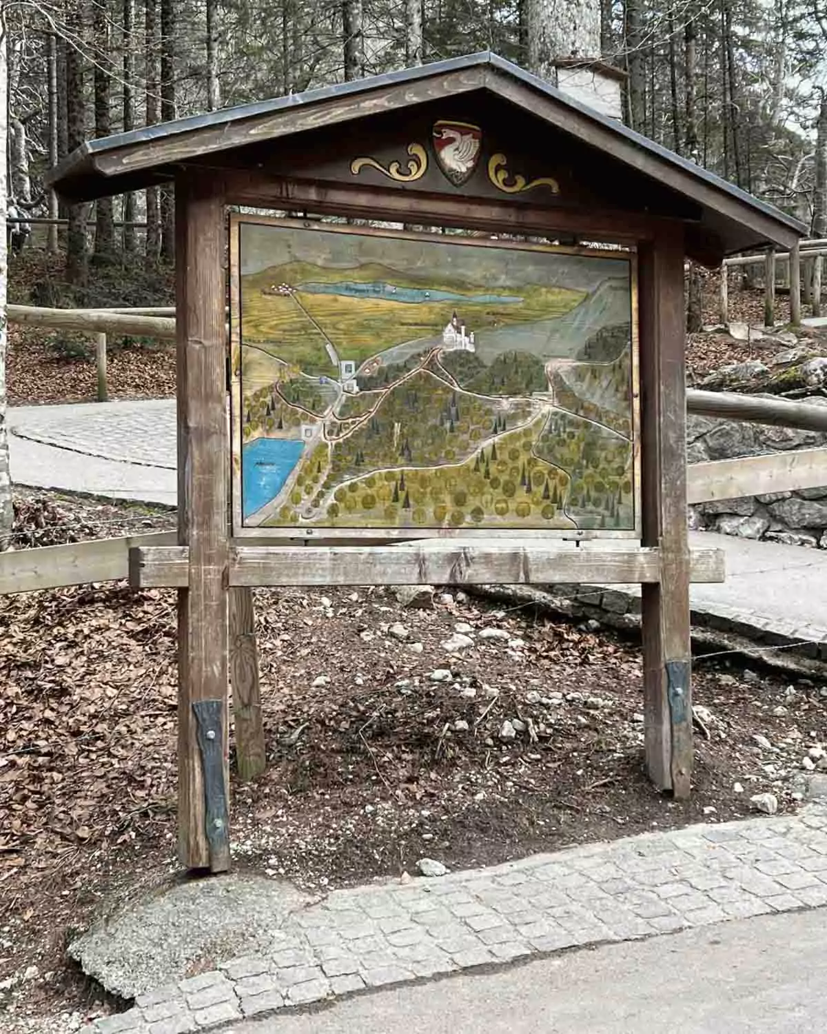 Informational sign displaying a detailed map of Neuschwanstein Castle grounds, including walking paths, shuttle stops, Marienbrücke, and nearby Hohenschwangau Castle.