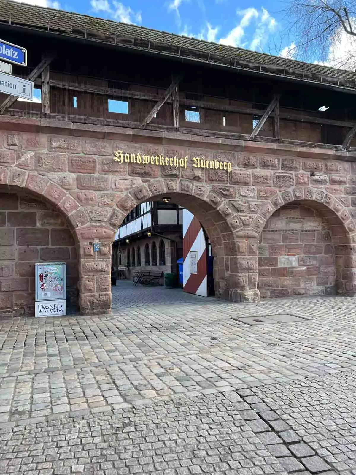Arched stone entrance to Handwerkerhof Nuremberg, framed by medieval walls and signage, leading into the charming artisan courtyard with half-timbered shops.
