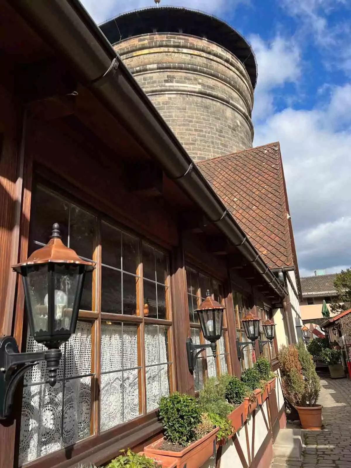 Handwerkerhof Nuremberg nestled against the medieval city walls, with a round stone tower rising above half-timbered artisan shops and cobblestone paths.