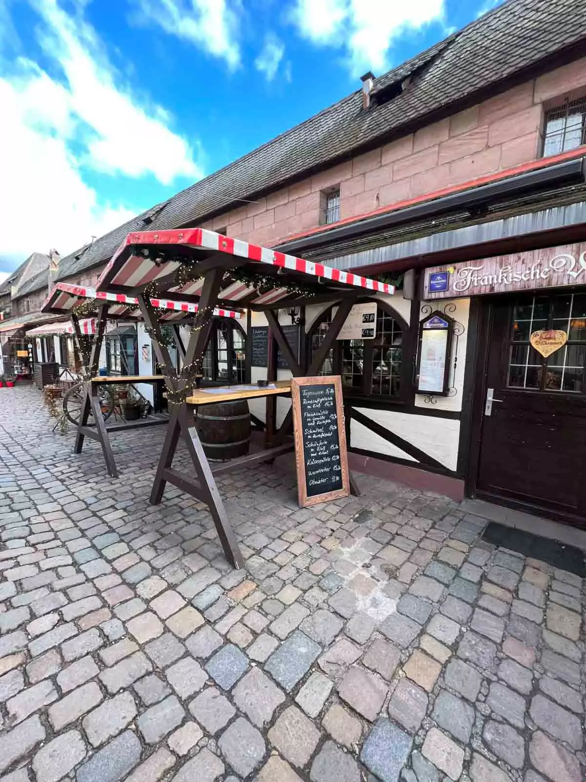 Handwerkerhof in Nuremberg, Germany, featuring rustic wooden picnic tables set among charming half-timbered buildings and artisan stalls within the historic courtyard near the old city walls.