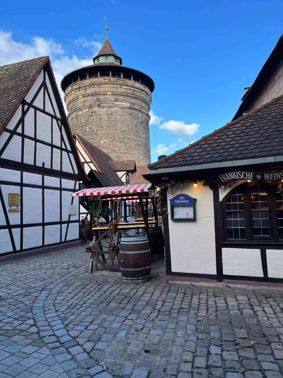 Handwerkerhof Nuremberg nestled against the medieval city walls, with a round stone tower rising above half-timbered artisan shops and cobblestone paths.