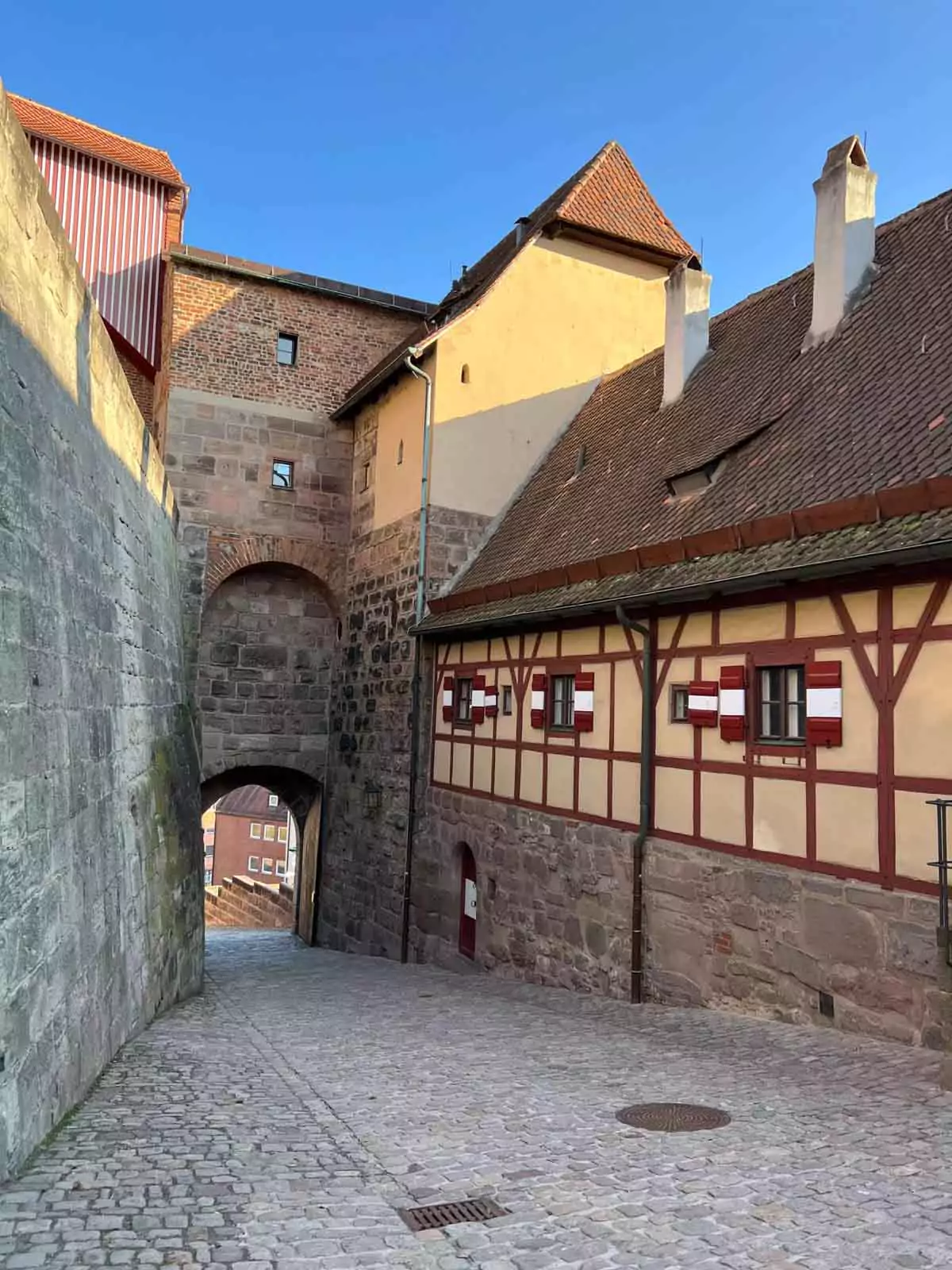 A stone courtyard within the walls of Nuremberg Imperial Castle, showing the arched main entrance flanked by tall stone walls and medieval architectural details. The historic setting reflects the castle’s defensive design and heritage.