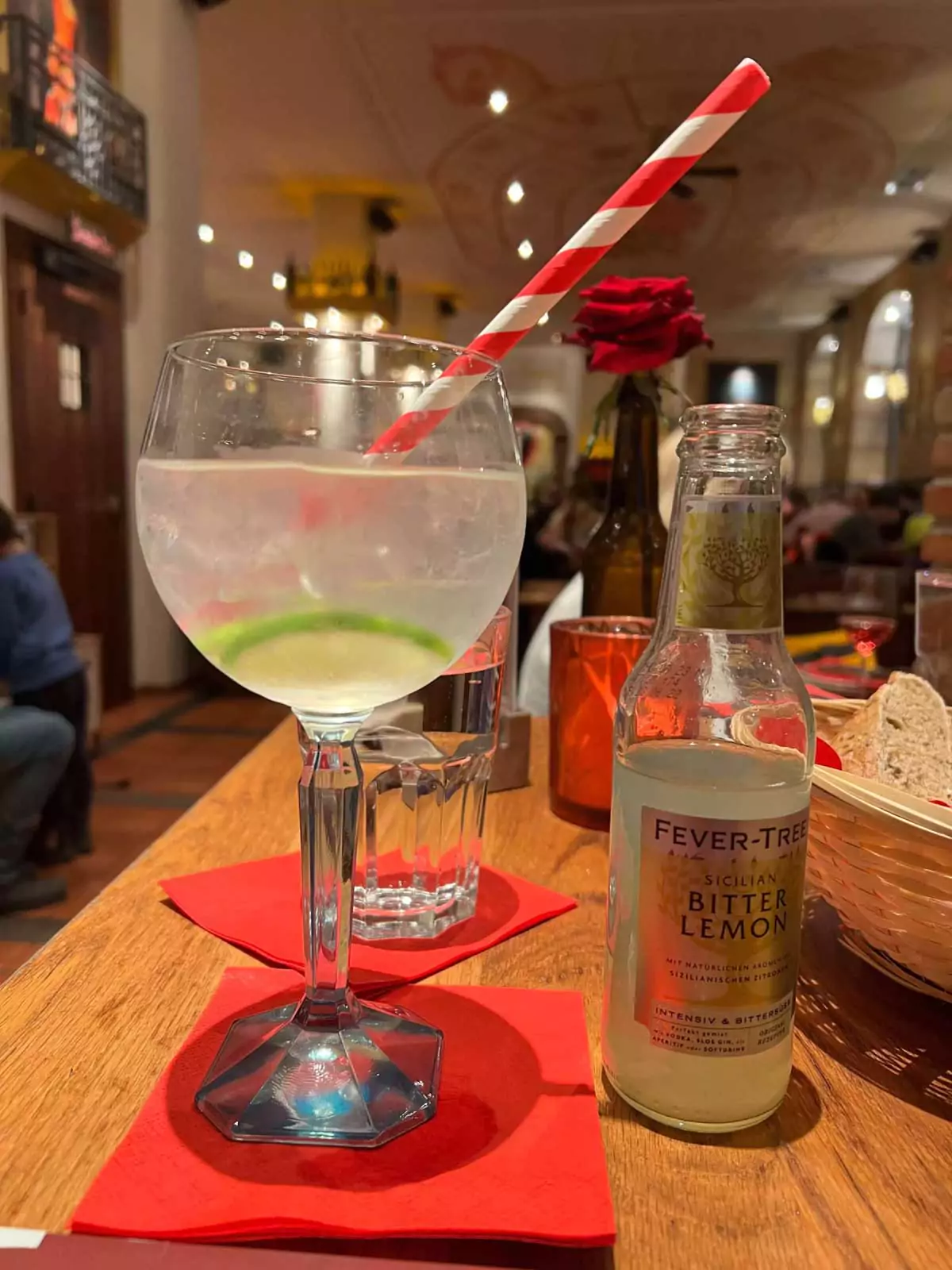 "Gin and tonic served on a table at Tapasitos, with a crisp clear glass, ice, lime wedge, and botanical garnish, set against a lively dining atmosphere — a refreshing cocktail