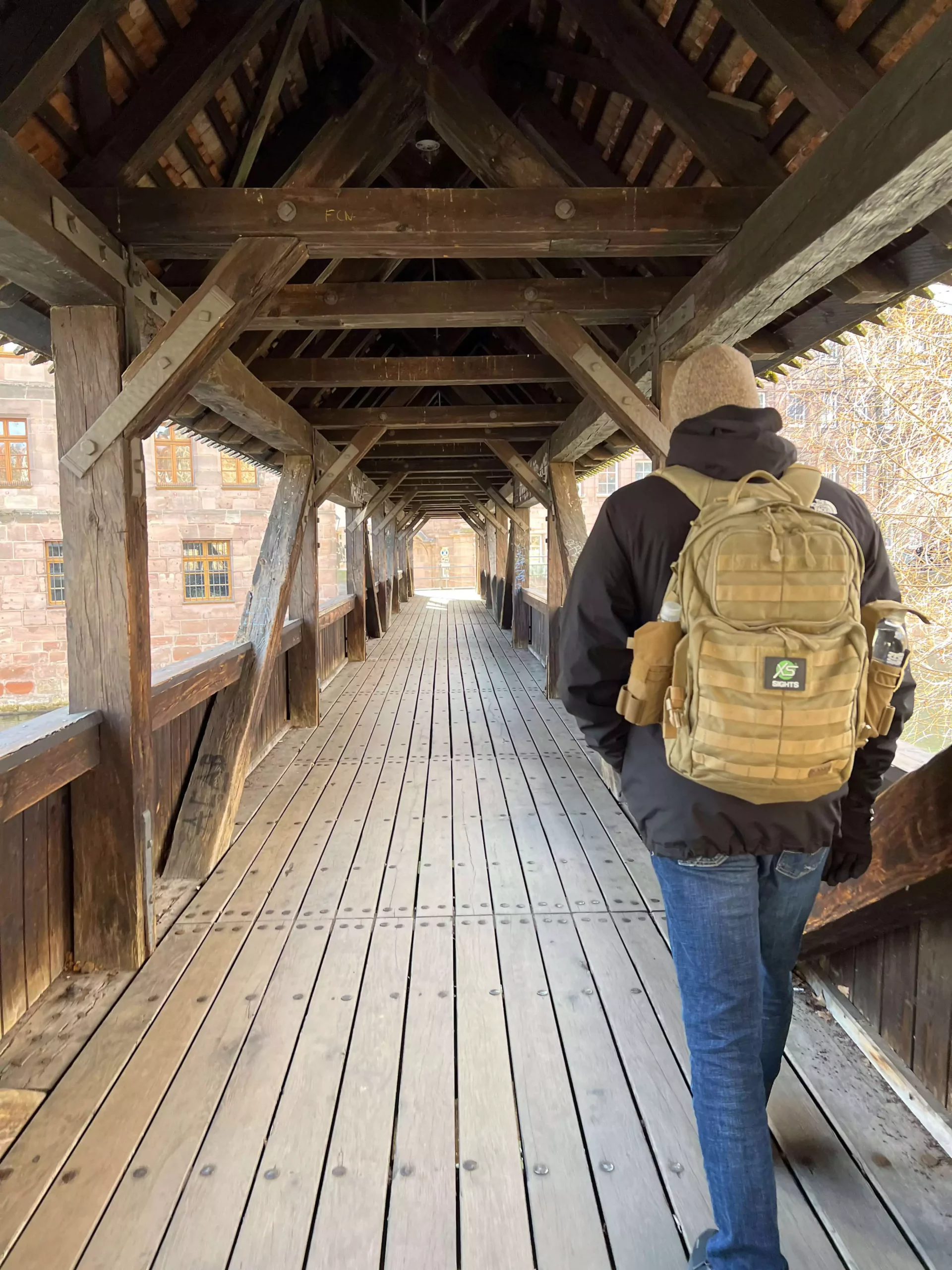 Zack walking across Hangman’s Bridge (Henkersteg) in Nuremberg, Germany, a historic covered wooden footbridge crossing the Pegnitz River, with timber-framed buildings and stone towers nearby.