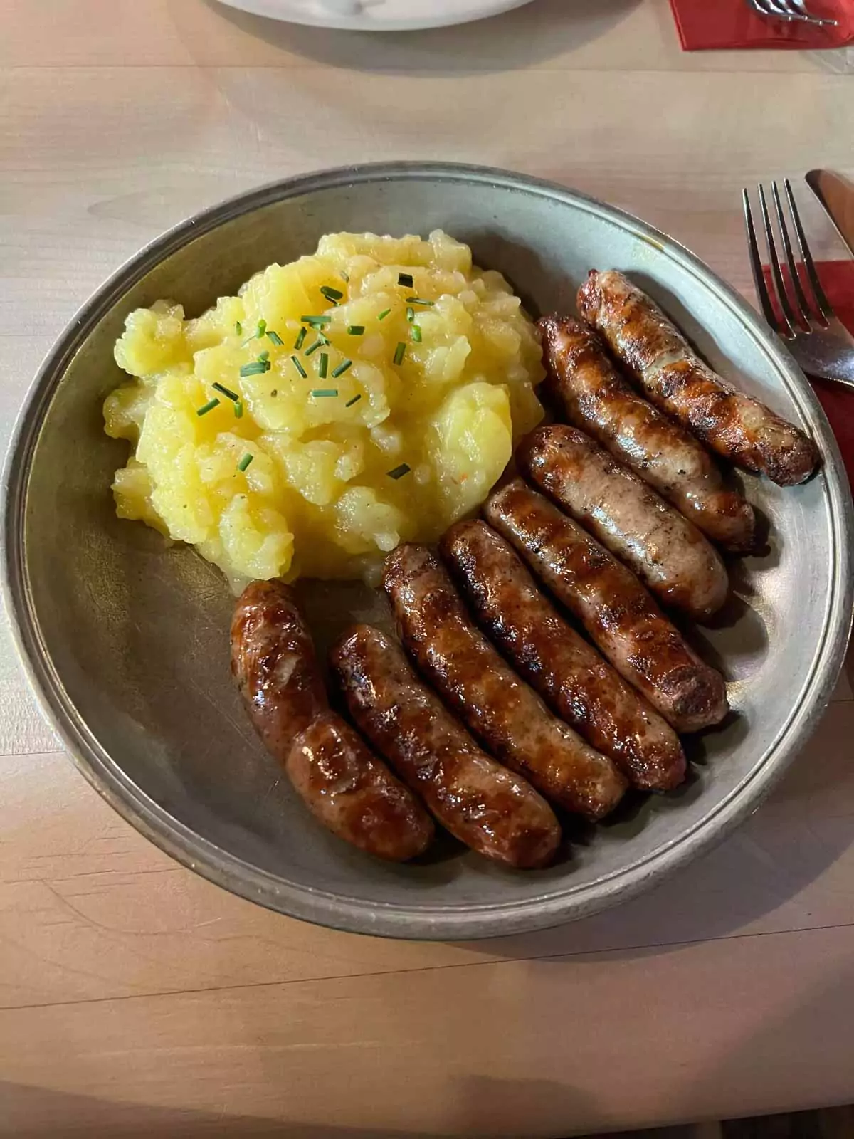Traditional Franconian meal at Zum Gulden Stern in Nuremberg, Germany, featuring grilled Nürnberger sausages served with a side of creamy potato salad on a rustic plate.