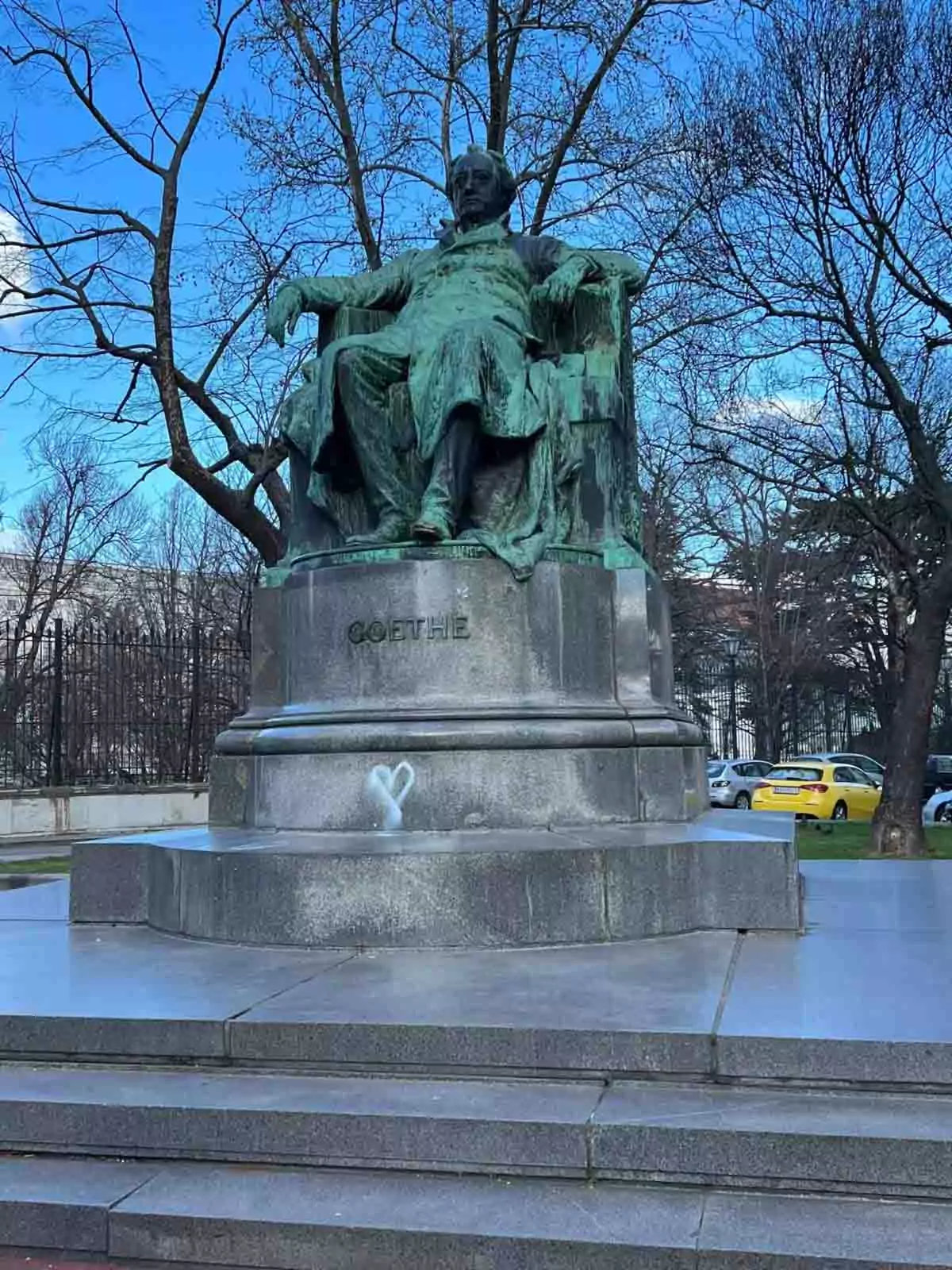 Bronze statue of Johann Wolfgang von Goethe in Vienna, Austria, seated in a dignified pose atop a stone pedestal, surrounded by greenery in a peaceful city park.