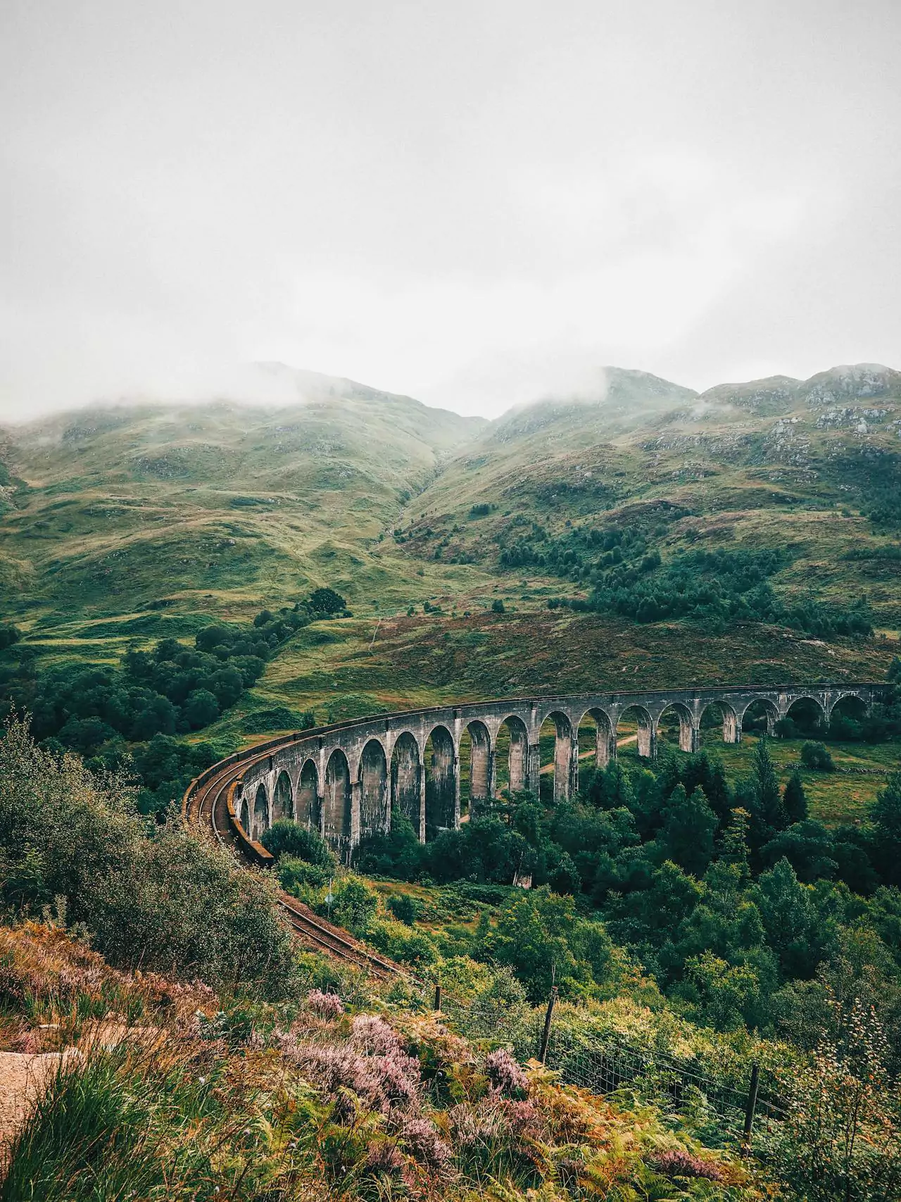Glenfinnan Viaduct in Scotland, known from the Harry Potter films, with its sweeping stone arches curving through the lush green Highlands, often pictured with the Hogwarts Express crossing above.