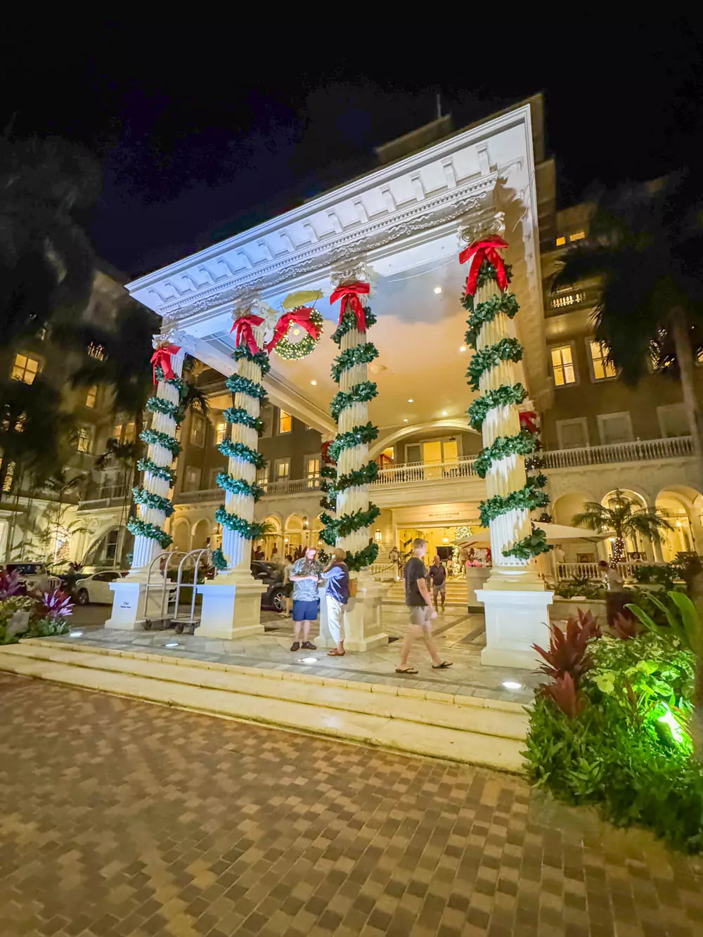 Festively decorated entrance of the Moana Surfrider, The Grande Dame of Waikīkī, adorned with holiday garlands, wreaths, and twinkling lights along its historic white columns.