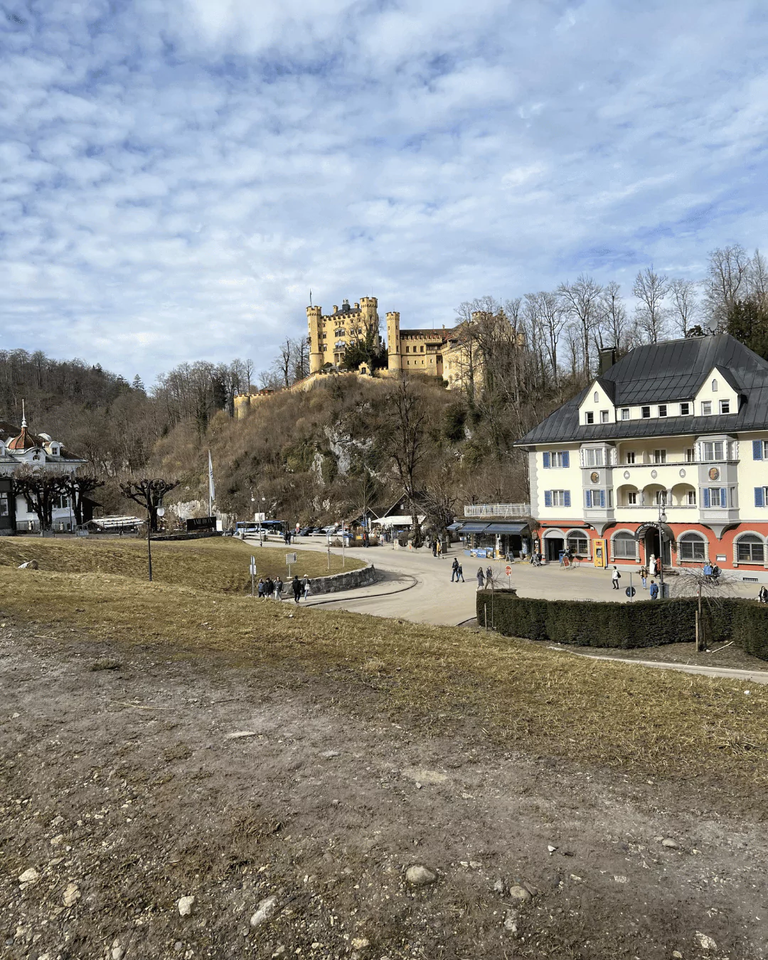 Hohenschwangau Castle perched on a forested hill above Schwangau Village in Bavaria, Germany, with its yellow façade and towers overlooking the alpine landscape below.