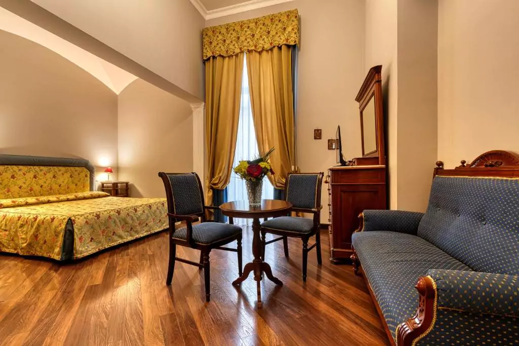 Interior of a bedroom at Decumani Hotel De Charme in Naples, Italy, featuring a regal bed with tufted headboard, rich drapery, antique furnishings, and warm ambient lighting