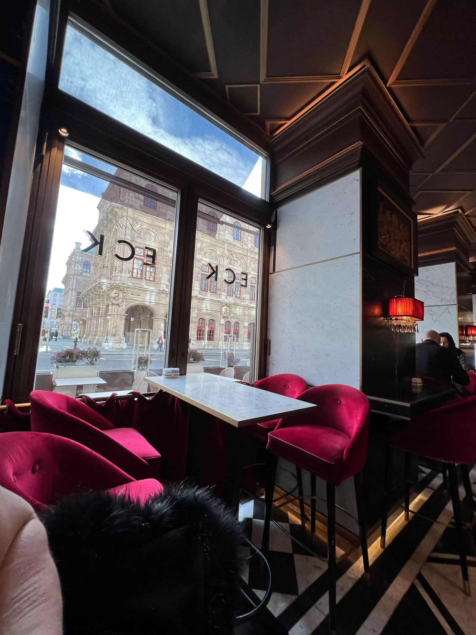 An interior table at Café Sacher in Vienna, Austria, surrounded by plush red velvet chairs and set with fine china. The elegant décor and rich textures reflect the café’s classic Viennese charm and timeless sophistication.