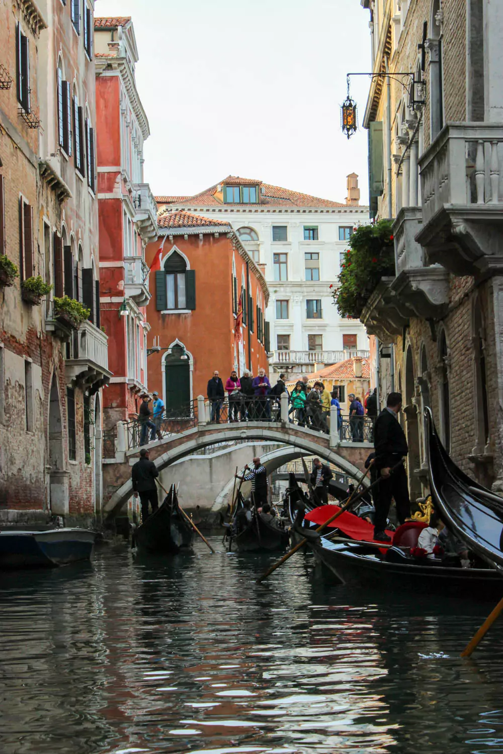 View from a gondola ride through a canal in Venice, Italy, with historic buildings rising along the water’s edge, arched pedestrian bridges overhead, and gentle ripples trailing behind the gondola.