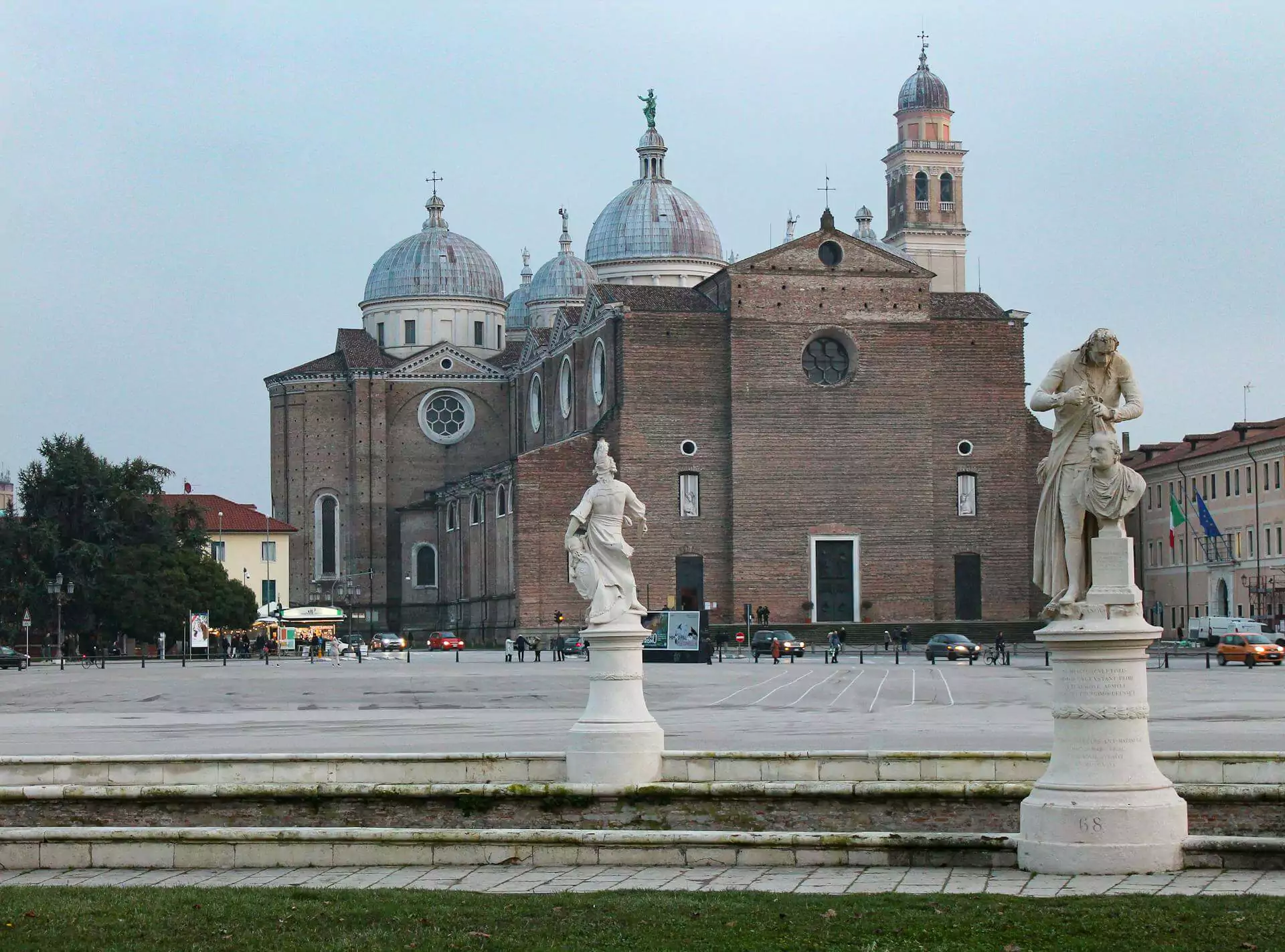 Abbey of Santa Giustina in Padua, Italy, featuring its expansive brick façade, domed rooflines, and bell towers, set in a peaceful square near the Prato della Valle with a blend of Renaissance and Baroque styles.