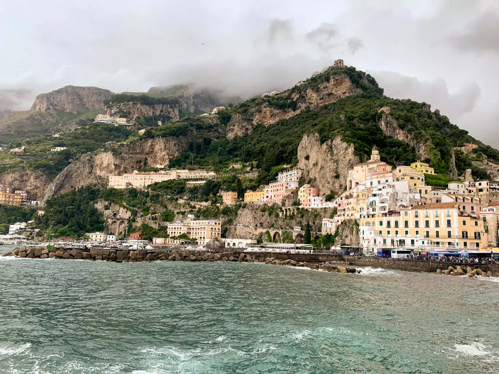 a view of Amalfi town in the Amalfi Coast with green mountains in the background and clouds in the sky