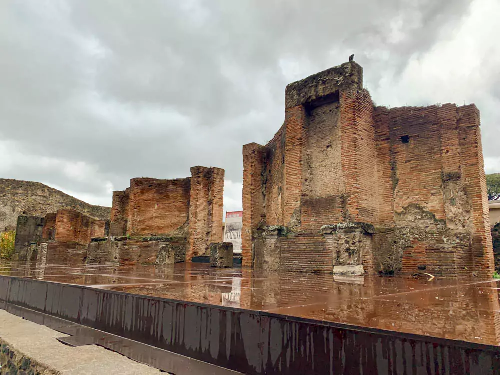 The Large Theatre in the Archaeological Park of Pompeii, Italy, on a cloudy day, with ancient stone seating curving around the stage and overcast skies adding a dramatic tone to the historic Roman amphitheater.
