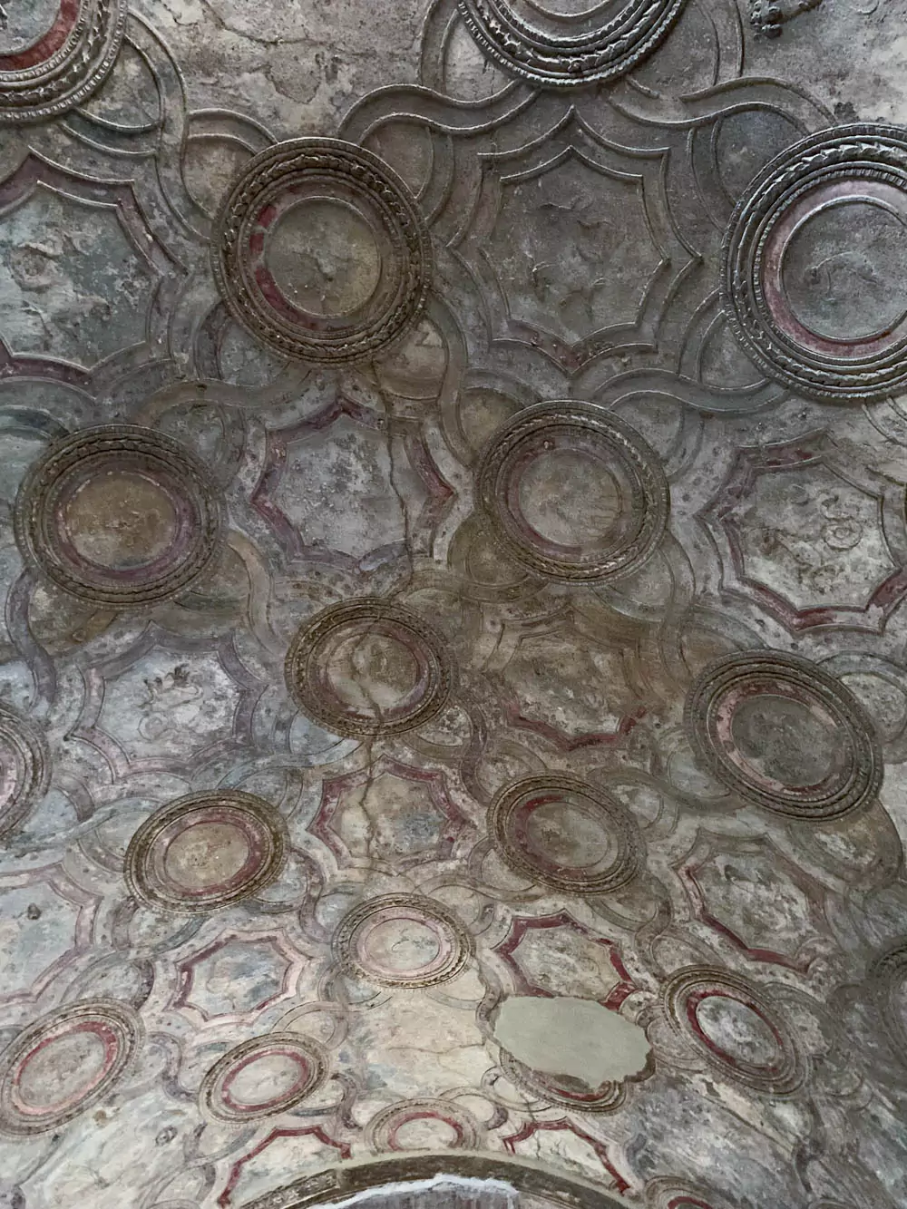 View inside the Stabian Baths (Terme Stabiane) at the Archaeological Park of Pompeii, looking across a vaulted, decorated ceiling toward the west wall of Vestibule 1, showcasing preserved Roman architectural and artistic detail.