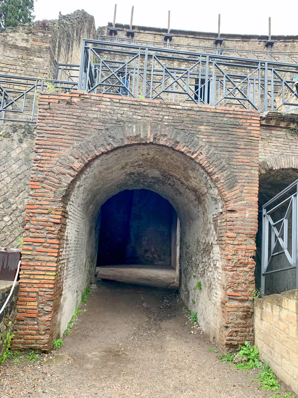 Facades at the outlet of the western aditus of the Great Theatre of Pompeii, featuring weathered stone walls, arched doorways, and remnants of Roman architectural detailing that once framed the entrance and exit for spectators.