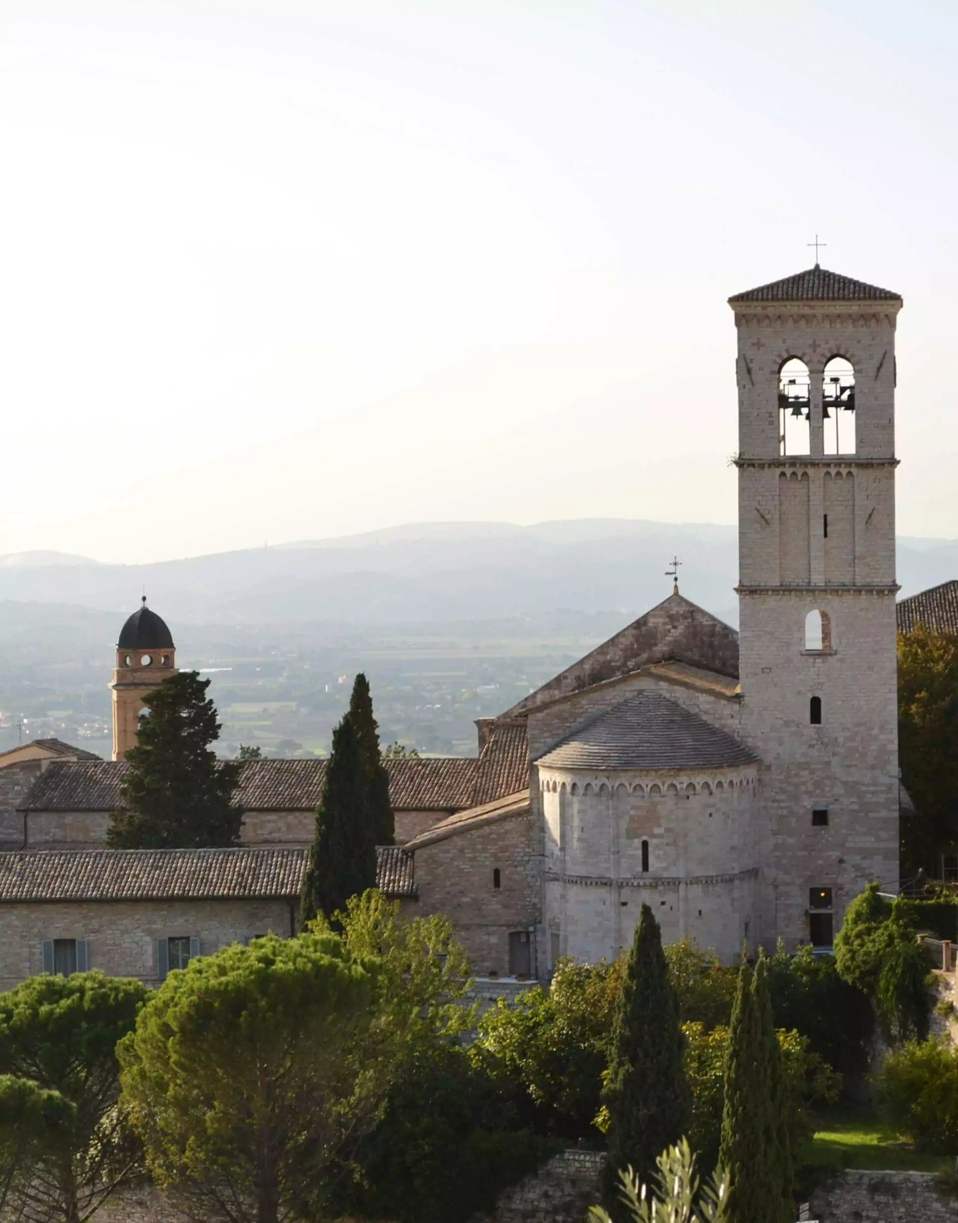 Basilica of Saint Francis of Assisi in Italy, photographed by Glen Mc Call, featuring the church’s layered stone façade and bell tower perched on a hillside, overlooking the Umbrian valley under a clear sky.