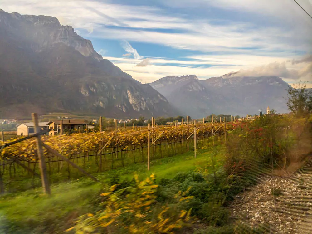 Stunning view of the Dolomites in Italy as seen from a train window, with jagged mountain peaks rising above green valleys and alpine villages, framed by the train’s interior.