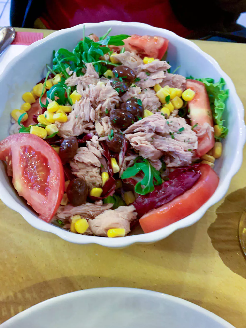 Plate of tuna salad at a restaurant in Burano, Italy, featuring fresh greens, chunks of tuna, tomatoes, and olives, presented in a bright and colorful dining setting.